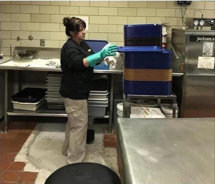 Servpro employee wiping down trays in a large commercialized kitchen